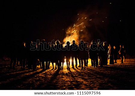 People standing next to a big beach bonfire with sparks flying around