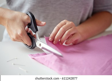 people, stitching, needlework, sewing and tailoring concept - woman with tailor scissors or shears cutting out fabric at studio