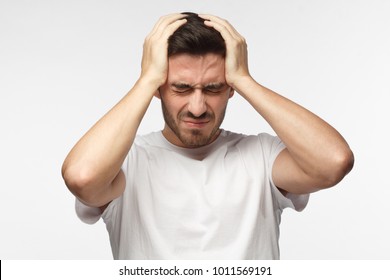 People, stress, tension and migraine concept. Upset unhappy young man squeezing head with hands, suffering from headache. 