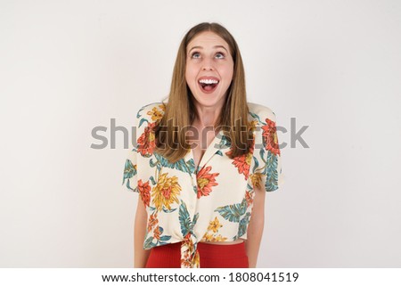 People and sudden reaction concept. Surprised caucasian beautiful female student, shrugs shoulders, looking sideways, being happy and excited about new plans with friends. Isolated over gray wall.