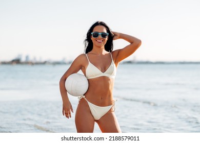 people, summer and leisure concept - happy smiling young woman in bikini swimsuit posing with volleyball on beach - Shutterstock ID 2188579011