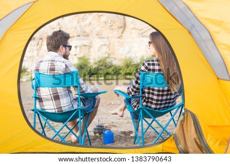 people, summer tourism and nature concept - young couple drinking tea near tent
