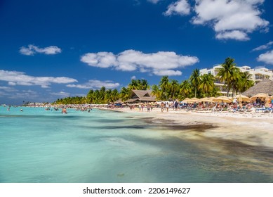 People Sunbathing On The White Sand Beach With Umbrellas, Bungalow Bar And Cocos Palms, Turquoise Caribbean Sea, Isla Mujeres Island, Caribbean Sea, Cancun, Yucatan, Mexico.