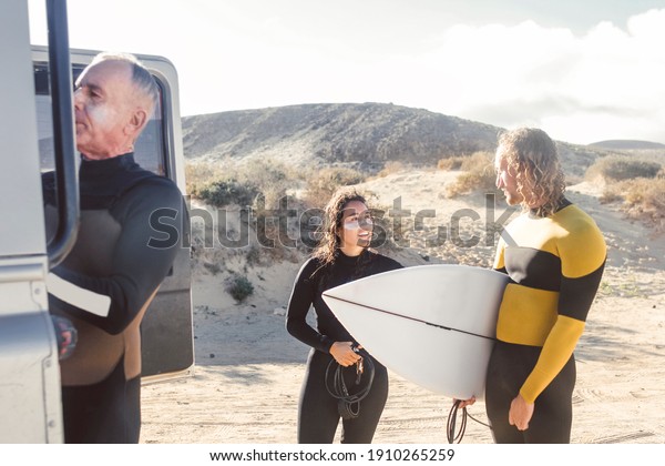People from a surf school getting\
ready to go surfing in the sea- People wearing wetsuits to go into\
the water - Three friends picking up surfboards from the\
car