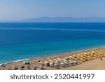 People swimming, sunbathing or doing other activities on the Elli Beach  in Rhodes Island, Greece. Group of colorful umbrellas on the sand.  Mountains on the horizon.