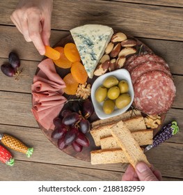 People Taking Food From Appetizer Board With Cheese, Nuts, Fruits, Toasts And Charcuterie Over Wooden Table.