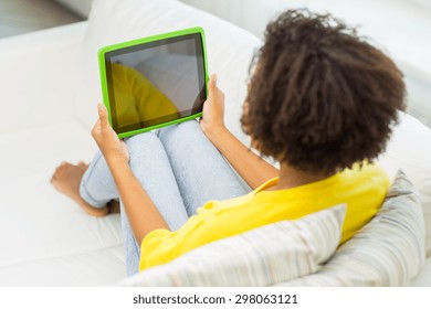 People, Technology, Advertisement And Leisure Concept - Happy African American Young Woman Sitting On Sofa With Tablet Pc Computer Black Blank Screen At Home