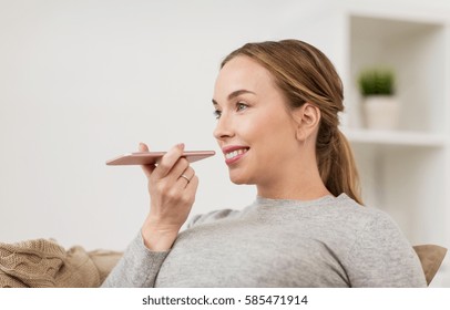 People, Technology, Communication And Leisure Concept - Happy Young Woman Using Voice Command Recorder Or Calling On Smartphone At Home