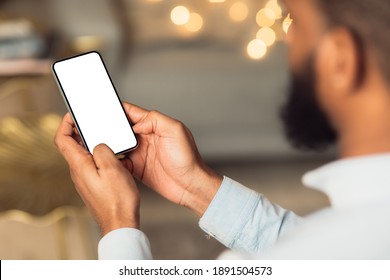 People And Technology Concept. Over The Shoulder View Of Unrecognizable African American Man Using Smart Phone With White Empty Screen For Mockup, Sitting At Home, Making Video Call Or Chatting