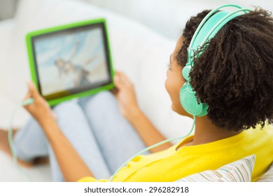 People, Technology And Leisure Concept - Close Up Of Happy African American Young Woman Lying With Tablet Pc Computer And Headphones Listening To Music And Watching Video At Home