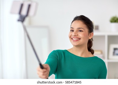 People, Technology And Lifestyle Concept - Happy Woman Taking Picture With Smartphone Selfie Stick Or Monopod At Home