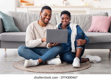 People And Technology. Portrait Of Positive Black Family Of Two People Using Laptop Computer, Watching Video Or Movie, Shopping In Online Store, Sitting On The Floor Carpet In Living Room At Home