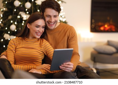 People And Technology. Portrait Of Smiling Beautiful Couple Holding And Using Digital Tablet Sitting On Couch Indoors In Living Room. Happy Family Surfing Internet Choosing Gift, Watching Movie Online - Powered by Shutterstock