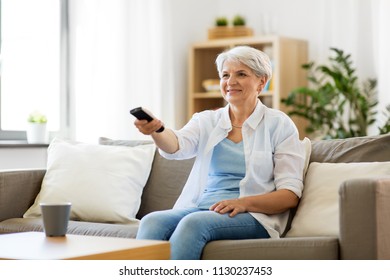 People, Television And Entertainment Concept - Senior Woman In Eyeglasses With Remote Control Watching Tv At Home