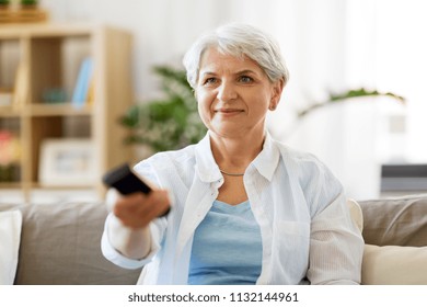 People, Television And Entertainment Concept - Senior Woman In Eyeglasses With Remote Control Watching Tv At Home