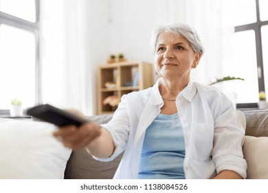 People, Television And Entertainment Concept - Senior Woman In Eyeglasses With Remote Control Watching Tv At Home