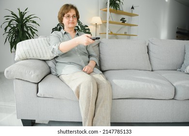 people, television and entertainment concept - senior woman in eyeglasses with remote control watching tv at home. - Powered by Shutterstock