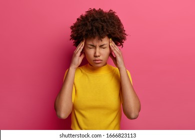 People, Tiredness, Medicine, Symptom Concept. Unhappy Distressed Ethnic Woman Has High Blood Pressure, Rubs Temples To Relieve Headache, Keeps Eyes Shut, Has Unbearable Migraine, Poses Indoor