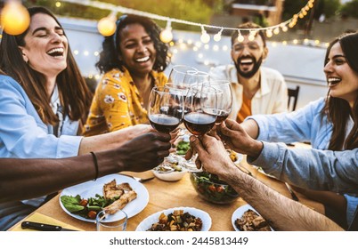 People toasting red wine glasses on rooftop dinner party - Happy friends eating meat and drinking wineglass at restaurant patio - Food and beverage lifestyle concept with guys and girls dining outdoor - Powered by Shutterstock