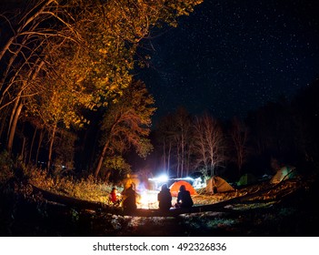 People Tourist At Camp In The Forest With Bonfire At Tent Around At Night Starry Sky