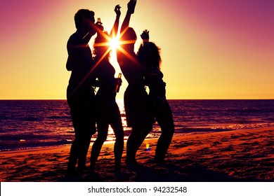 People (two Couples) On The Beach Having Party, Drinking And Having A Lot Of Fun In The Sunset (only Silhouette Of People To Be Seen, People Having Bottles In Their Hands With The Sun Shining Through)