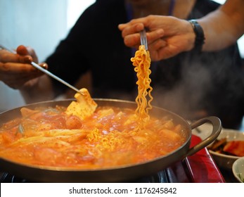 People Using Silver Chopsticks To Pick Up Noodles And Bean Curd From Hot Pot Of Budae Jjigae Or Korean Stew Made With Kimchi, Instant Noodle (ramyeon), Ham, Sausage, Tofu, Vegetables / Selective Focus