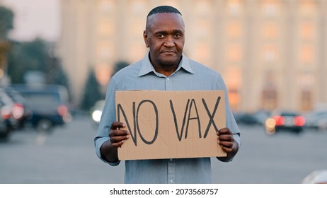 People Vaccination Phobia Concept. Adult Elderly African American Man Stands In City Street Holding Sign Banner With Text No VAX In Protest Of Unexamined Vaccine Against Covid 19 Stop Immunization