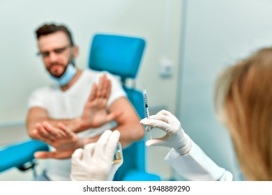 People Vaccination Phobia Concept. Female Doctor Trying To Give Vaccine To A Scared Patient. Angry And Distrustful Patient Refuses To Receive It. Stop Vaccinations. Say No To The Coronavirus Vaccines.