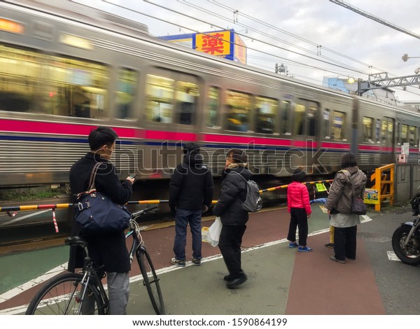 People waiting for a commuter\
train pass at Railway intersection. Tokyo, Japan. 12 December\
2019