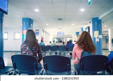 People In A Waiting Room Of Hospital, Men And Women Wait Their Turn 
