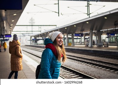 People waiting for train at railroad station. Smiling young woman looking at arriving train. Rail transportation in Vienna, Austria, Europe. Travel concept