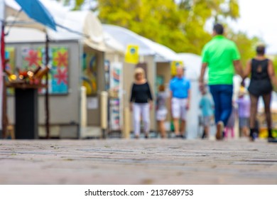 People walk around an art festival enjoying paintings and drawings in a downtown public park in this defocused photo. - Shutterstock ID 2137689753