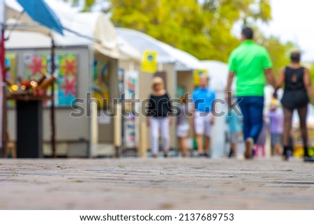 People walk around an art festival enjoying paintings and drawings in a downtown public park in this defocused photo.