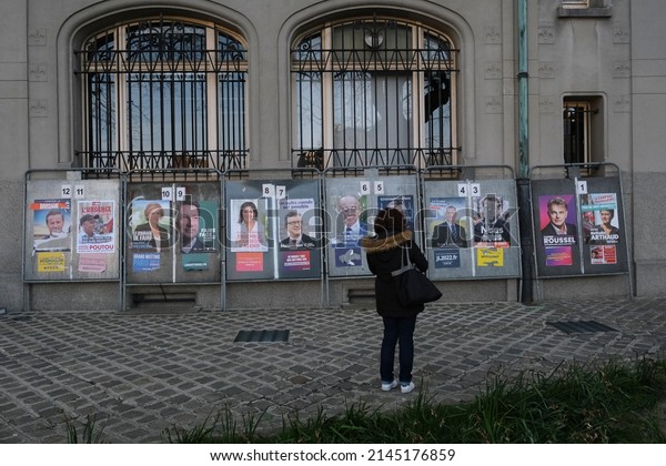 People walk in front of campaign posters on a board\
outside a polling station during the first round of France\
presidential elections at a polling station in Lille, France on\
April 10, 2022.