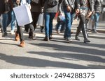 People walking in abstract urban scene depicting crowd of multicultural shoppers on a busy city street carrying bags on a sunny day. The pedestrians crossing the road are in shallow focus.