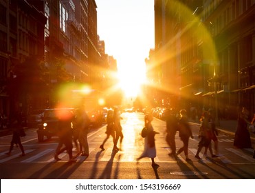 People walking across the street in New York City with the bright light of sunset shining between the buildings along 23rd St in Midtown Manhattan NYC
