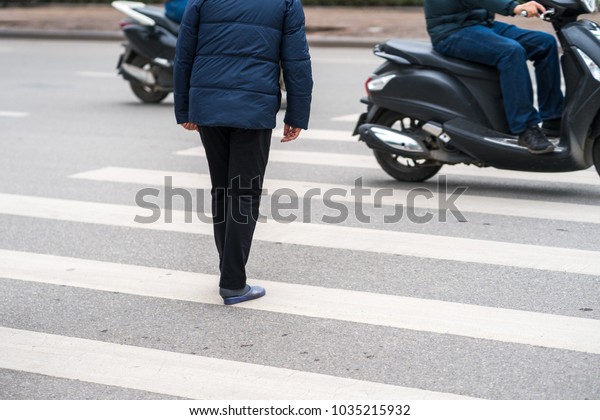 People walking across a street\
while motorbikes keep running on street in Hanoi, Vietnam.\
Closeup
