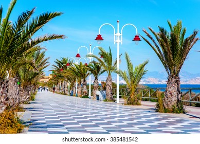 People walking along the seafront palm-lined promenade in Los Arenales del Sol. Costa Blanca, Spain