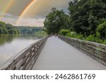 people walking down the boardwalk along the Chattahoochee river with vast silky brown river water surrounded by lush green trees at Roswell Riverwalk Boardwalk in Roswell Georgia USA	