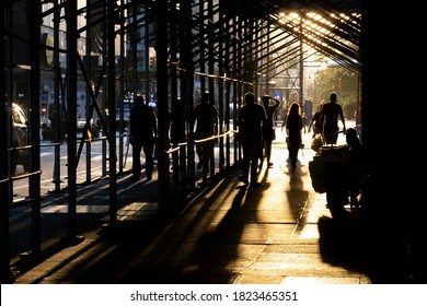 People Walking Down A Busy Sidewalk In New York City With Sunlight Shining Through The Construction Scaffolding Overhead 