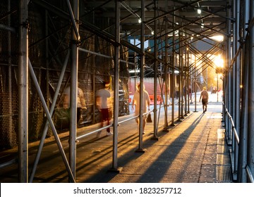 People Walking Down A Sidewalk In New York City With The Light Of Sunset Shining Through Construction Scaffolding Overhead