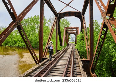 People walking on railroad tracks across bridge with river flowing underneath - Powered by Shutterstock