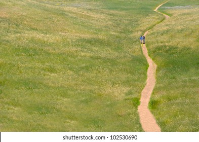 People Walking On A Trail In An Open Green Field