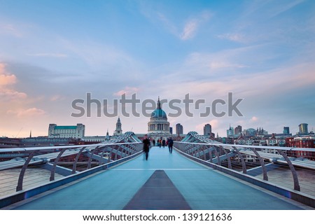 People walking over Millennium bridge at dusk. St Pauls cathedral in the background.