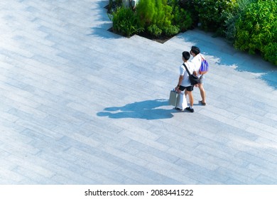 People Walking In The Street. Back Of Couple Man Walk Across On Concrete Pavement In Sunny Day. Summer Season Of Crowd Life. (wide Angle Of Aerial Top View)