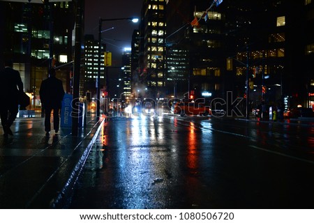 People walking Toronto streets at night in the rain, with lights reflecting in the puddles. A dystopian neo noir scene of red blue green and gold. Skyscrapers in the background and smoke from a grate.