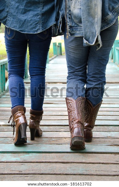 People wear jeans to wear boots walking on a wooden\
bridge.  
