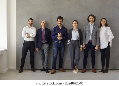 People Who Embody Success And Leadership. Group Portrait Of Happy Multi Aged Business Professionals After Meeting. Team Of Successful Company Employees Or Executives Standing Together Near Office Wall