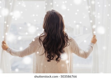 People, Winter, Christmas And Hope Concept - Close Up Of Happy Woman Opening Window Curtains At Home Over Snow