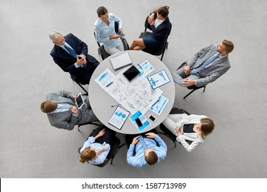 people, work and corporate concept - business team with gdgets and papers at round office table